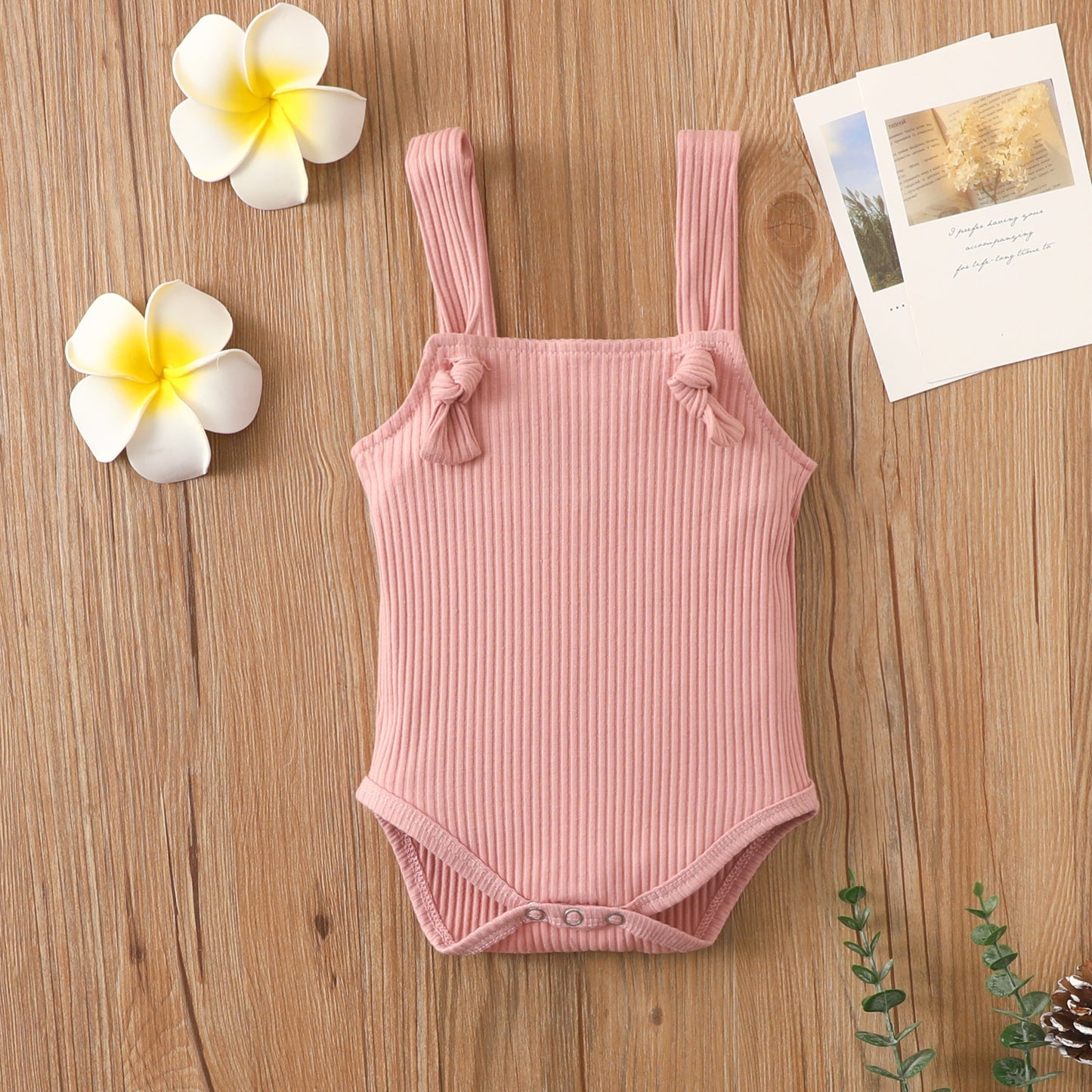 Côte & Crown soft cotton romper for babies in pink with strap and button closure on wooden background
