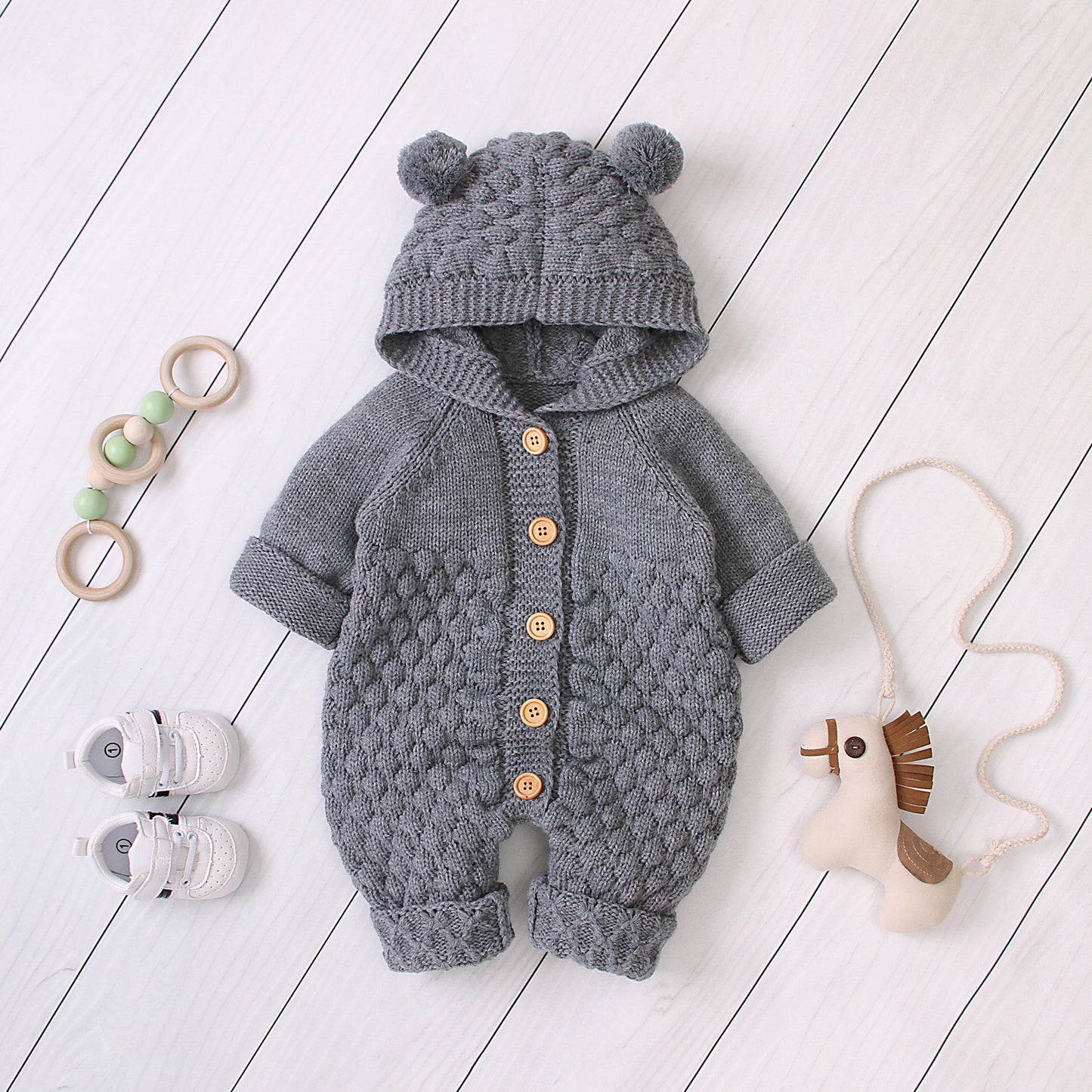 Côte & Crown gray knitted baby onesie with hood and bear ears, wooden button closure, styled with baby shoes and toys