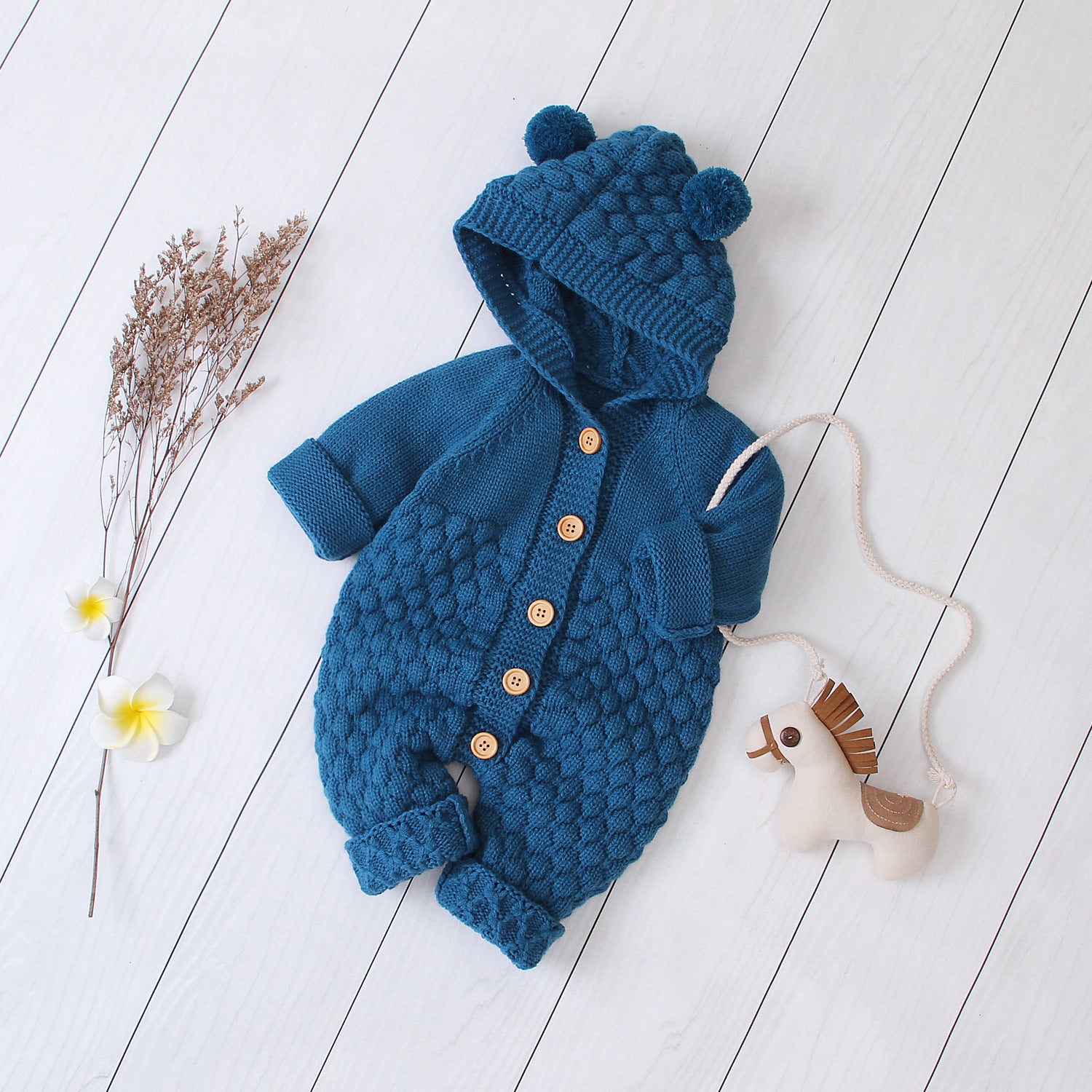 Côte & Crown blue knitted baby onesie with hood and pom-poms, wooden buttons, and textured pattern