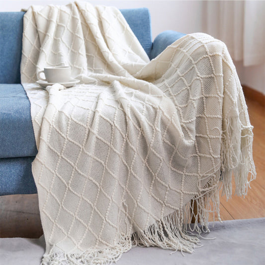 Cream-coloured affordable luxury throw blanket draped over a blue sofa with a mug on top
