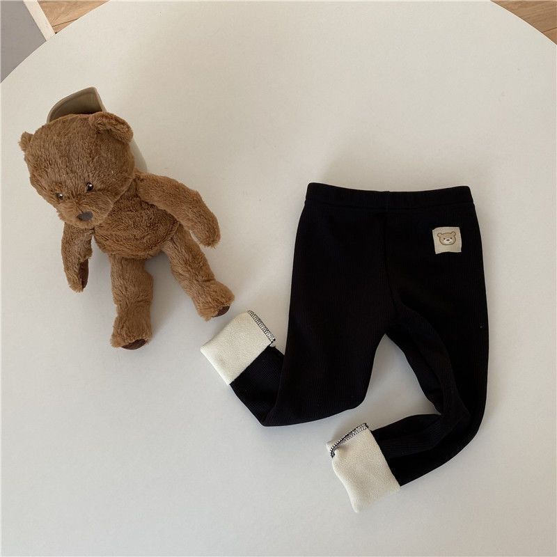 Côte & Crown black baby pants with white cuffs and teddy bear patch next to brown plush teddy bear
