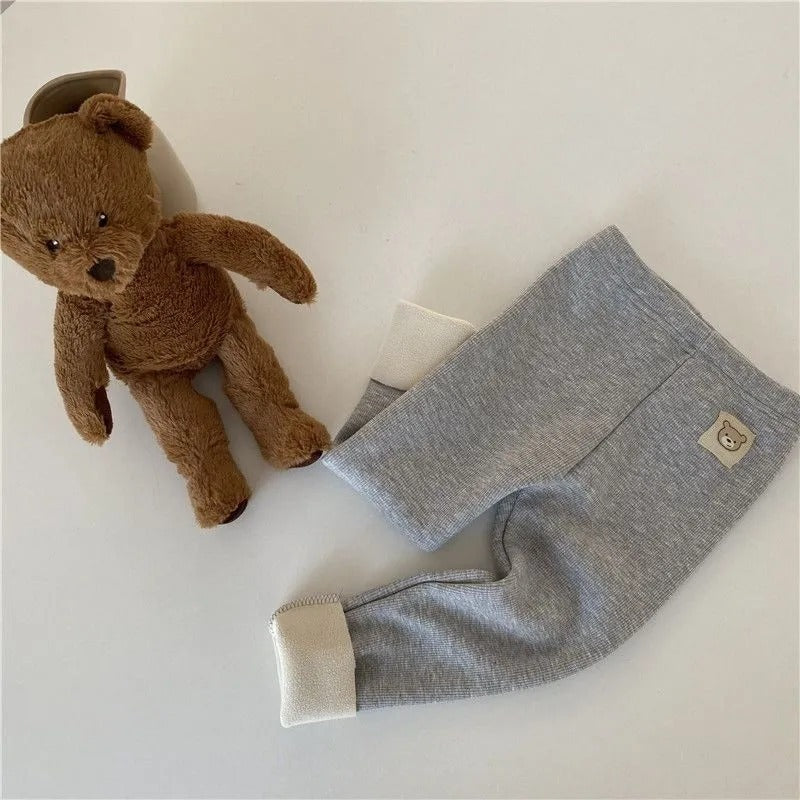 Côte & Crown gray baby pants with cream cuffs and teddy bear patch next to brown teddy bear plush