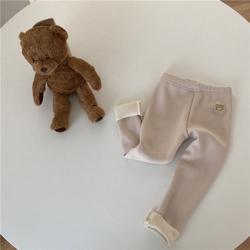 Côte & Crown beige baby pants with bear patch and cuffed legs next to a brown teddy bear toy