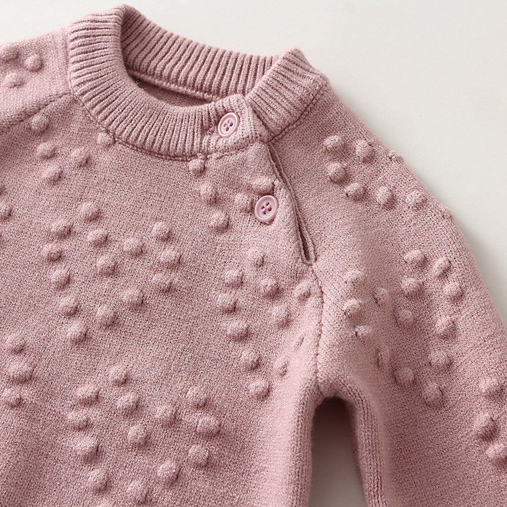 Close-up of pink children's knitted sweater set with textured bobble details and button closure