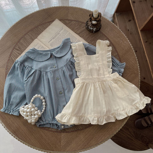 Côte & Crown ruffled baby romper dress in cream with a blue checkered blouse on a wooden table